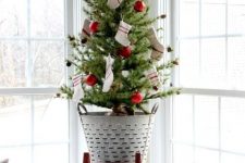 a fun tabletop Christmas tree decorated with red ornaments and striped stockings and put into a rustic bucket brings coziness
