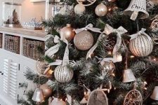 a glam rustic Christmas tree with taupe, grey and neutral ornaments, lights, bells, pinecones and bows and some carved wooden ornaments