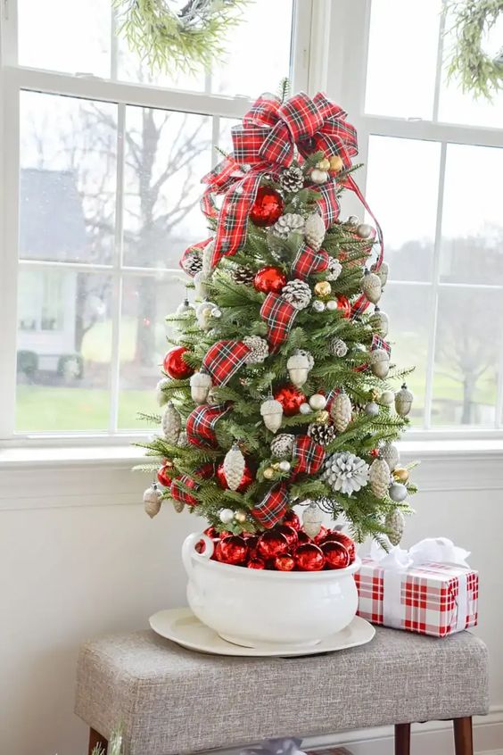 a lovely tabletop Christmas tree decorated with red and gold ornaments, pinecones and a red plaid bow on top