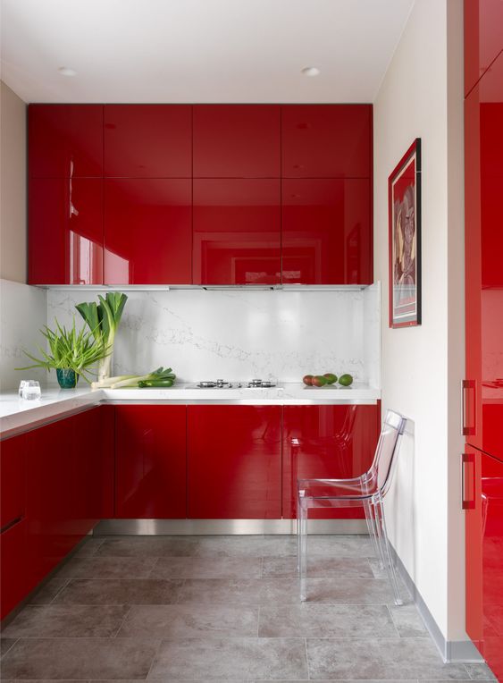 a minimalist deep red kitchen wotj a white stone backsplash and countertops and a sheer chair plus a bold artwork