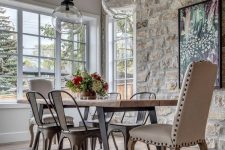 a modern French country kitchen with a stone accent wall, a wooden table and metal chairs and a leather chair plus pendant lamps
