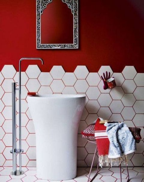 a modern and bold red and white bathroom with hex tiles, red walls and red grout, a tall sink standing and a hand holder
