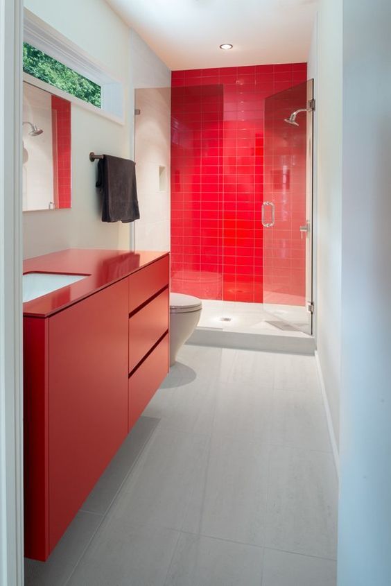 a modern bathroom with a red tile wall in the shower, a red sleek vanity and minimalist glass doors and a mirror