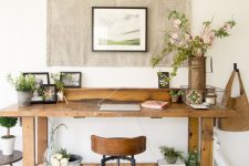 a modern farmhouse home office with a large wooden desk, an artwork on the wall, a wood and metal chair and baskets and plants