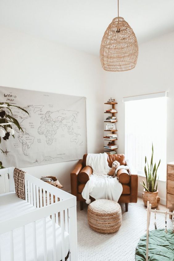 a neutral boho nursery with a map on the wall, a leather chair, a pendant lamp, a white crib, a shelving unit and a wooden dresser