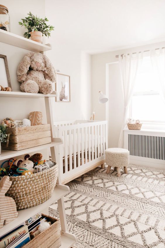 a neutral boho nursery with white furniture, a Moroccan rug, a shelving unit and white textiles is very cozy and chic