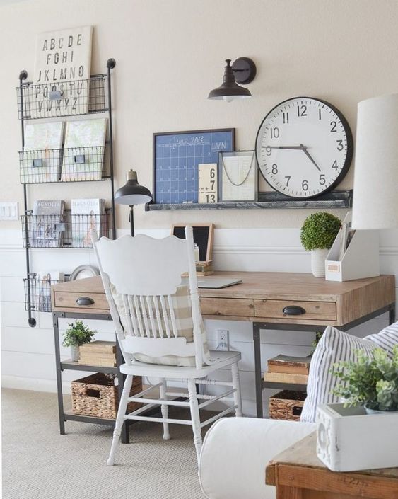 a neutral rustic home office with a wooden and metal desk, a metal box shelving unit, an open shelf with artworks and a round clock