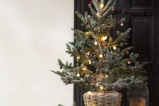 a pretty tabletop Christmas tree with lights and red and gold tiny ornaments placed in a basket for a rustic space