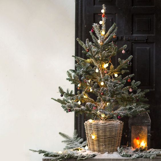 a pretty tabletop Christmas tree with lights and red and gold tiny ornaments placed in a basket for a rustic space