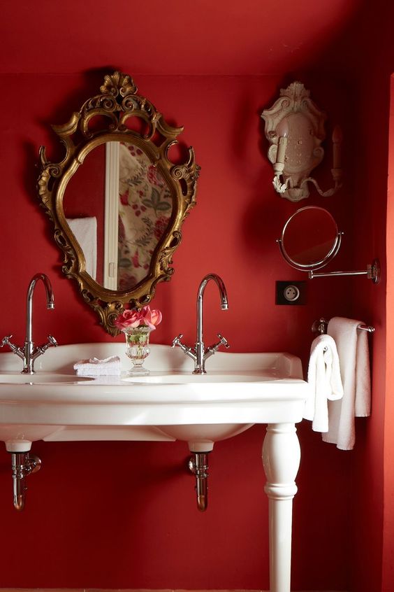 a refined and chic vintage red bathroom with a double sink vanity, a refined mirror, white towels and sconces