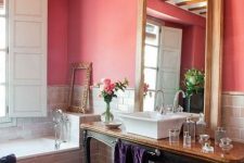 a refined red bathroom with grey tiles walls and a clad bathtub, a refined crystal chandelier and an exquisite vintage vanity table
