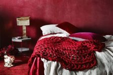a refined red bedroom with a red plaster wall, a red rug, neutral, fuchsia and red bedding and a chic lamp