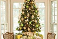 a refined tabletop Christmas tree decorated with green, gold and metallic ornaments and an oversized creamy bow on top