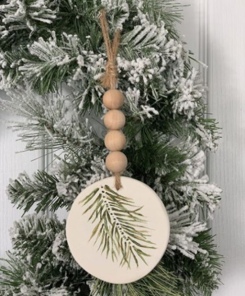 a rustic Christmas ornament of a wood slice with painted evergreens, wooden beads and twine