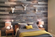 a rustic bedroom with a reclaimed wooden accent wall, simple furniture, faux taxidermy and grey and mustard bedding