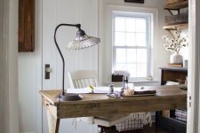a rustic home office with a woven rug, a wooden trestle desk, wooden shelves and a wooden console table plus a mesh chandelier
