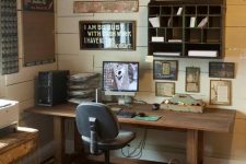 a shabby rustic home office with plank walls, wooden furniture, a gallery wall with artworks and a storage piece and a bucket as a trash can