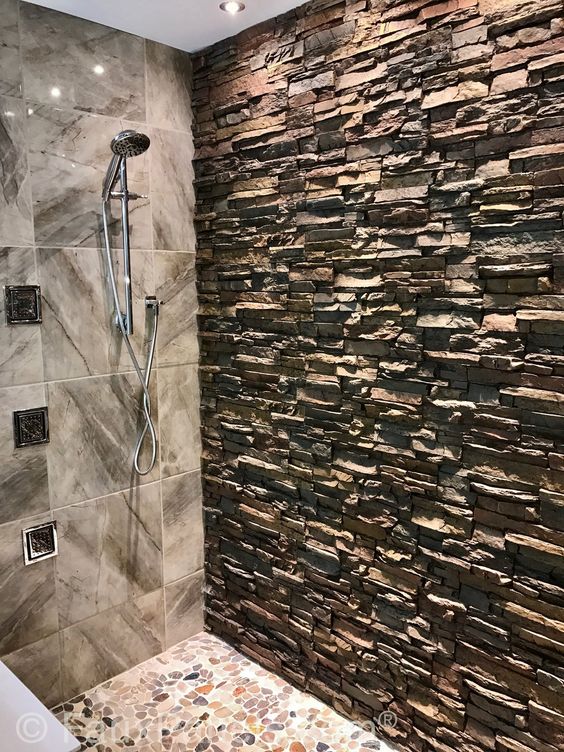a shower space with pebbles on the floor, grey marble tiles and an accent wall of manufactured stone for a warm feeling here