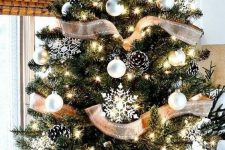 a simple rustic Christmas tree with white ornaments, snowy pinecones, snowflakes and lights