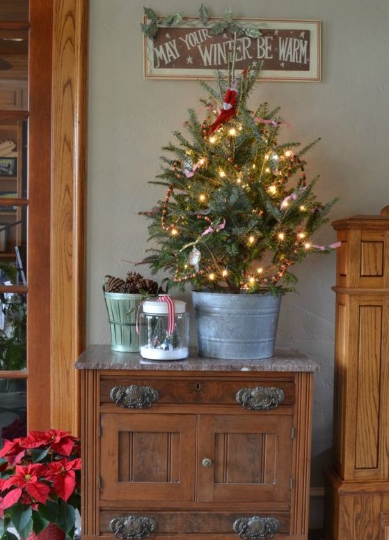 a small Christmas tree in a galvanized bathtub, decorated with lights, berries and a couple of ornaments