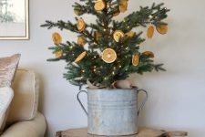 a small Christmas tree in a galvanized pot, with citrus and lights is a cool idea for a rustic space