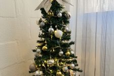 a small and pretty tabletop Christmas tree with lights and gold and silver ornaments plus a silver glitter bow on top