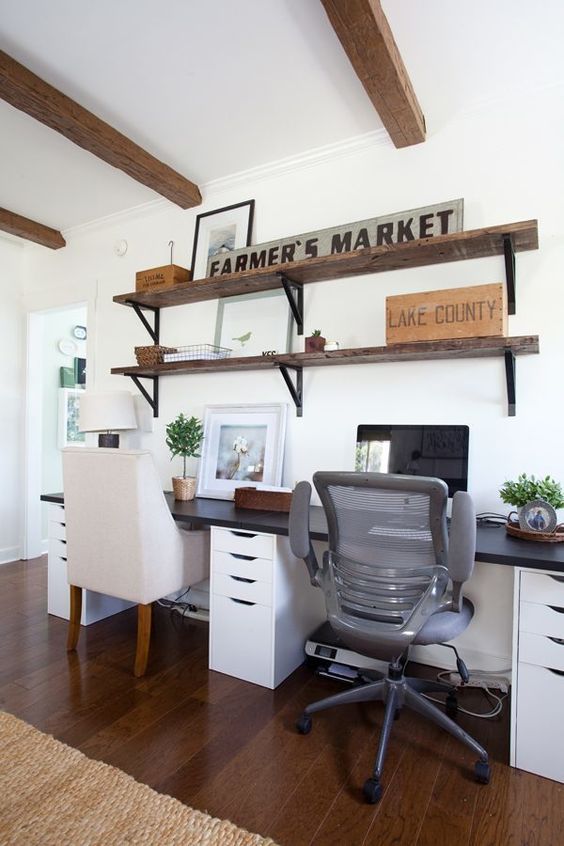 a small farmhouse shred home office with a black and white shared desk, rustic shelves on the wall and mismatching chairs for comfort