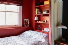 a small niche bedroom with red walls, built-in shelves, printed bedding and a curtain for privacy is very chic
