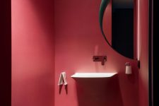 a small red powder room with a round lit up mirror, a floating vanity, a marble tile floor is modern and very chic and stylish