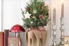 a small tabletop Christmas tree with apples, bells, snowflakes, cinnamons wrapped in burlap