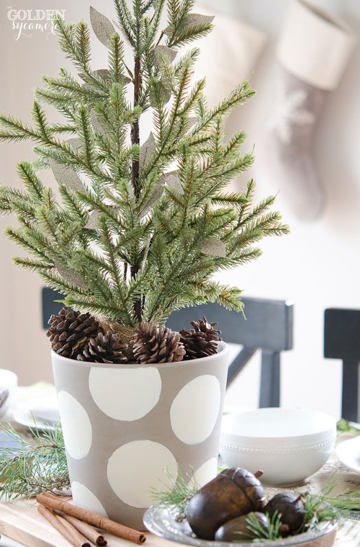 a stylish and simple tabletop Christas tree in a polka dot planter with pinecones is a cool and catchy decor idea
