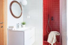 a stylish contemporary bathroom with a lainate floor, a red tile shower space, a round mirror and a floating vanity of white color