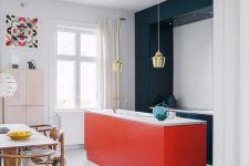 a stylish contemporary kitchen with sleek navy cabinets and a red kitchen island plus white countertops and gold pendant lamps