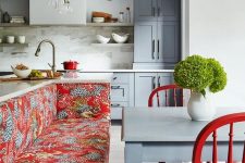 a stylish grey kitchen with a marble tile backsplash, a red upholstered bench and chairs plys some cookware for bold accents