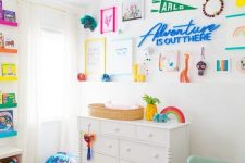 a super bold nursery with white furniture, a mint rocker, a bright gallery wall with artworks, signs and other stuff, a bold rug and books
