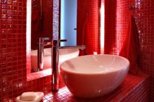 a super bright red bathroom fully clad with mini tiles, a round sink, some modern appliances and round lights here and there