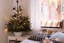 a tabletop Christmas tree styled with purple ornaments and lights is a cool solution for a Scandinavian space