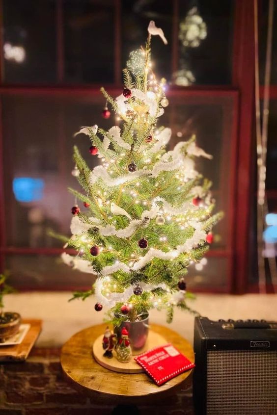 a tabletop Christmas tree with lights, tiny red ornaments and a tinsel garland is a cool and catchy idea