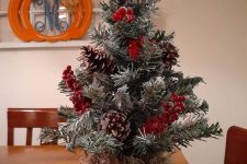 a tabletop Christmas tree with pinecones, berries and a red bow on top is a cool and catchy decoration