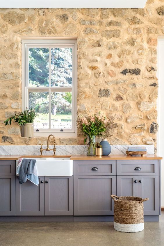 a tan stone accent wall contrasts the lilac cabinets creating a very eye catchy kitchen with a refined vintage feel