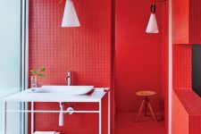 a total red bathroom all clad with tiles, with pendant lamps, an ethereal white vanity and a wooden stool in the shower