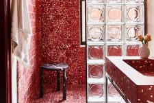 a unique bathroom with a red terrazzo shower space separated with a glass divider, a red terrazzo sink and a black marble stool