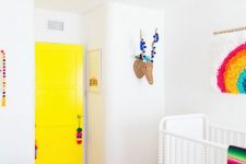a vibrant nursery with a sunny yellow door, bold printed bedding, a turquoise chandelier and bold artworks and garlands