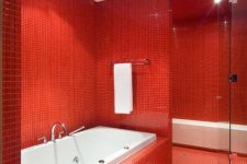 a vibrant red and white bathroom with white appliances and a white bench in the shower space plus red tiles covering the walls and floor