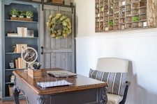 a vintage farmhouse home office with a grey vintage desk, a matching storage unit, a white chair and a large storage piece on the wall