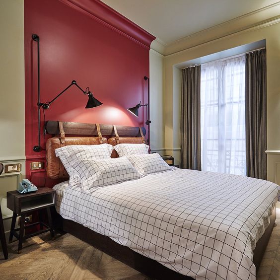 a vintage-inspired bedroom with a red accent wall, vintage furniture and metal sconces, windowpane bedding and simple curtains