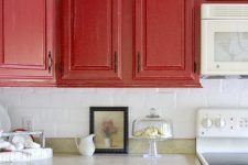 a vintage red kitchen with a white tile backsplash, stone countertops and white appliances and vintage handles is chic