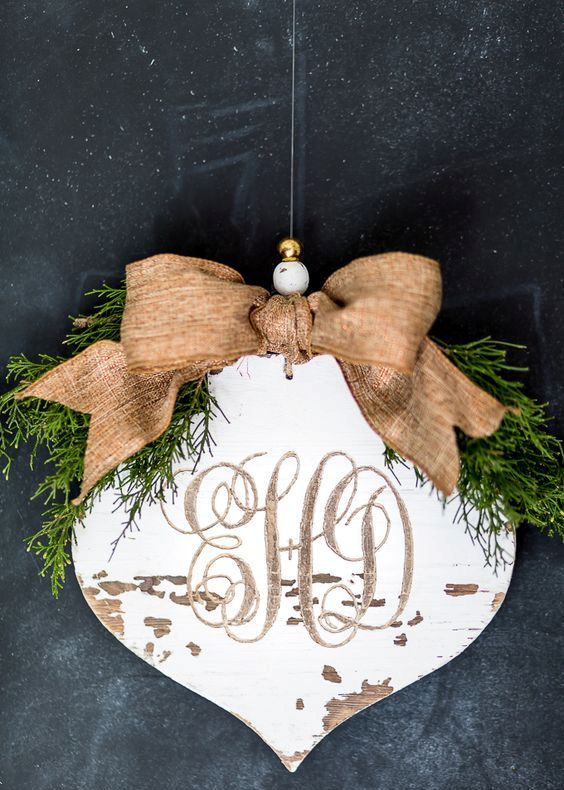 a vintage rustic Christmas ornament of a wooden plaque with calligraphy, a burlap bow and greenery on top