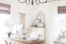 a vintage rustic home office done in neutrals, with a trestle desk, wooden furniture, a metal and wood chandelier, woven shades and a macrame hanging