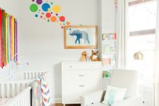 an airy and bright nursery with neutral walls and furniture, colorful textiles, fringe, rugs and some art on the wall